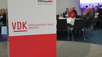 250411_Boeckler-Stiftung_Reitzig Banner der Böckler-Stiftung; im Hintergrund Konferenzteilnehmende